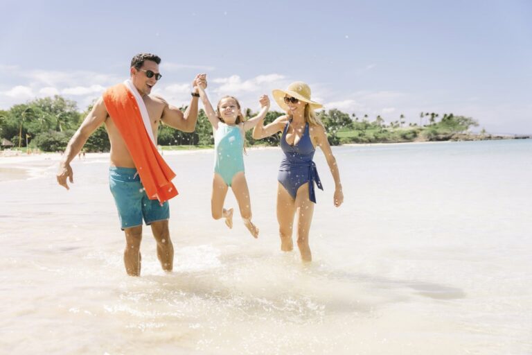 A joyful family of three running together along the shoreline, splashing in the ocean waves.