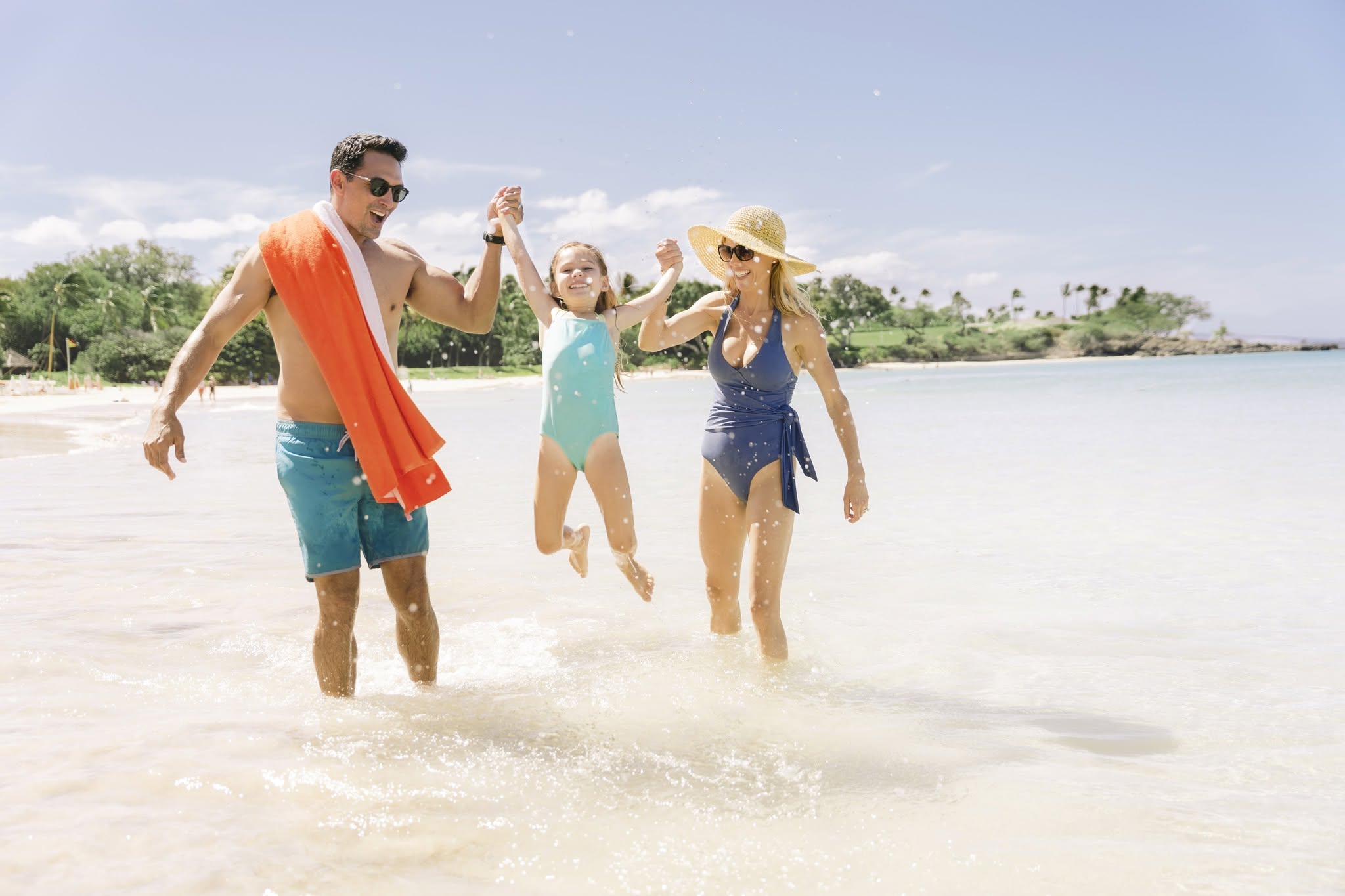A joyful family of three running together along the shoreline, splashing in the ocean waves.